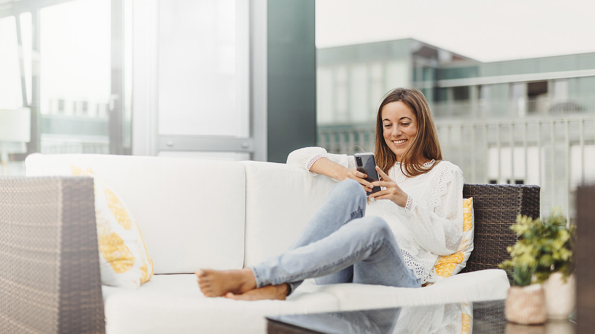 Eine Person sitzt auf einem Sofa, schaut auf ihr Smartphone und lächelt dabei.